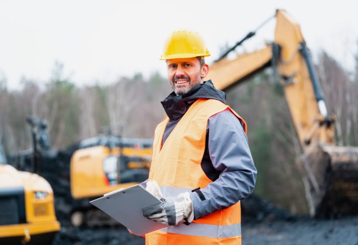 Portrait of a quarry worker standing in front of excavator smiling